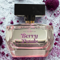 Thumbnail for Perfume bottle labeled 'Berry Petals' on a textured surface with purple flowers.