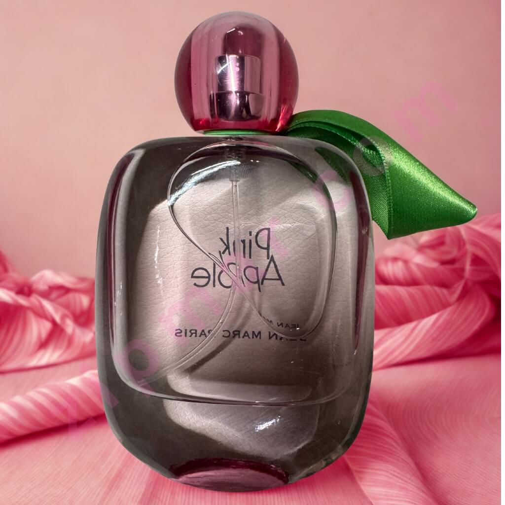 Perfume bottle with a green ribbon on a pink background