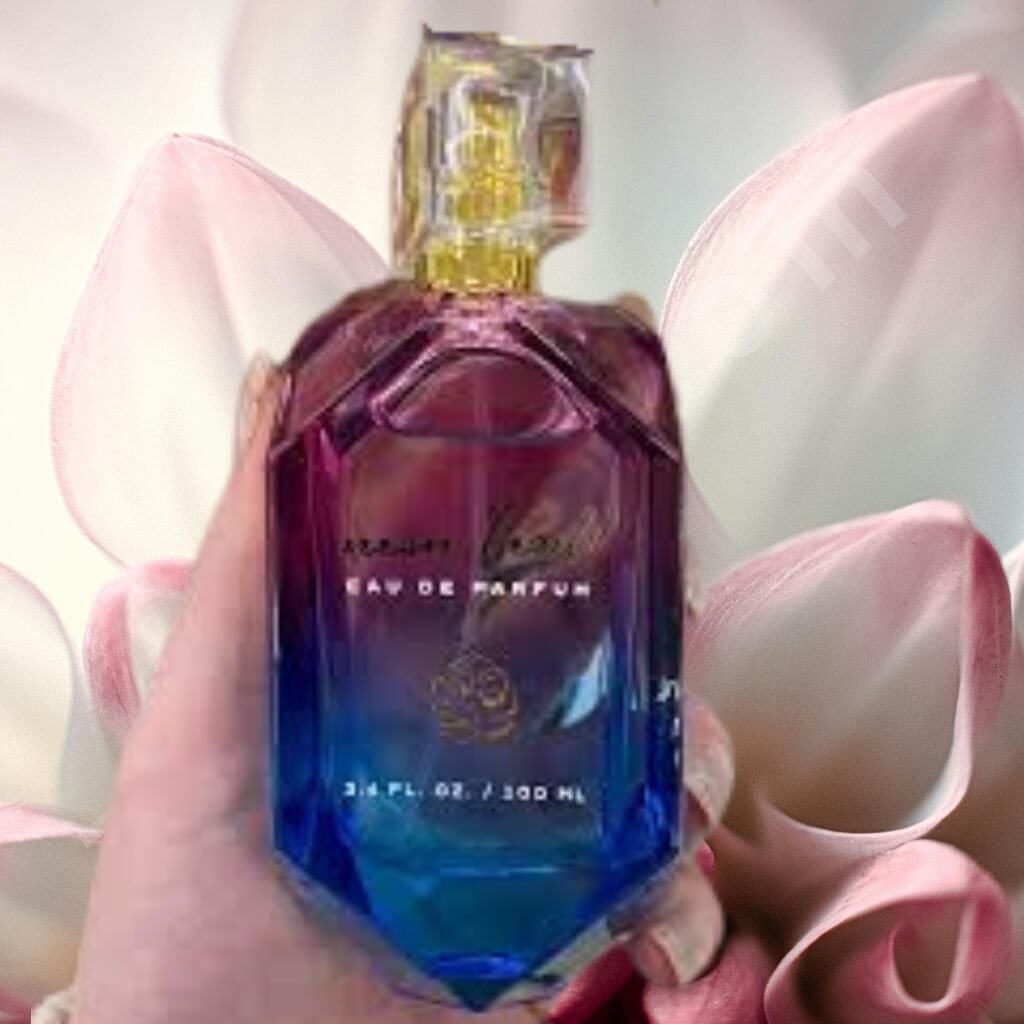 Blue perfume bottle held by a hand with pink flowers in the background