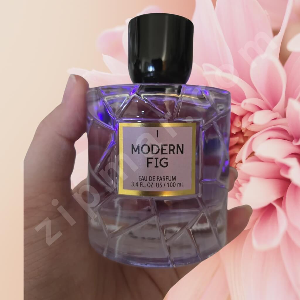 Perfume bottle labeled 'Modern Fig' held in front of pink flowers