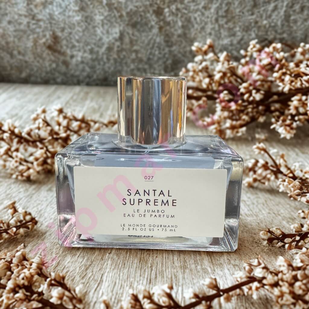 Perfume bottle labeled 'Santal Supreme' surrounded by dried flowers on a textured surface