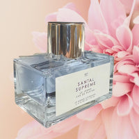 Thumbnail for Perfume bottle labeled 'Santal Supreme' with pink flowers in the background
