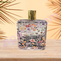 Thumbnail for Perfume bottle with floral design on a wooden surface and palm leaf background