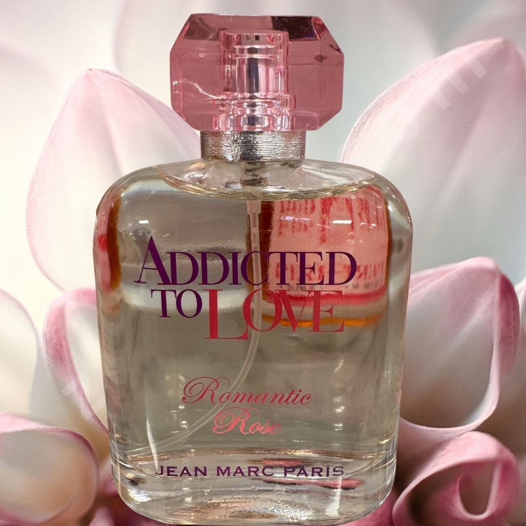 Perfume bottle labeled 'Addicted to Love Romantic Rose' by Jean Marc Paris with pink flowers in the background.