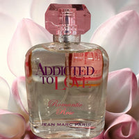 Thumbnail for Perfume bottle labeled 'Addicted to Love Romantic Rose' by Jean Marc Paris with pink flowers in the background.
