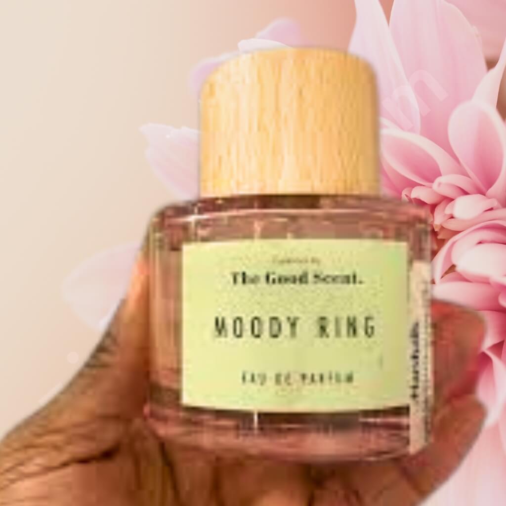 Perfume bottle labeled 'Moody Ring' held against a pink floral background