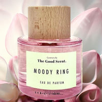Thumbnail for Pink eau de parfum bottle with wooden cap labeled 'Moody Ring' by 'The Good Scent' on pink floral background