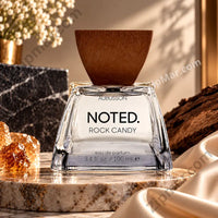 Thumbnail for Aubusson Noted Rock Candy Eau de Parfum 3.4 fl oz 100ml clear flared glass bottle with brown wood-grain inverted wedge cap and white label showing Aubusson Noted Rock Candy EDP clearly raw amber citrine crystal chunks dark mineral rock and cream satin silk on marble stone pedestal with white baby's breath flowers in gold vase in warm natural light background