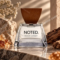 Thumbnail for Aubusson Noted. Rock Candy Eau de Parfum clear glass bottle with brown wooden wedge cap on stone marble surface surrounded by limestone rocks, rough bark pieces, dried white flowers and amber crystal rocks  warm natural editorial lifestyle