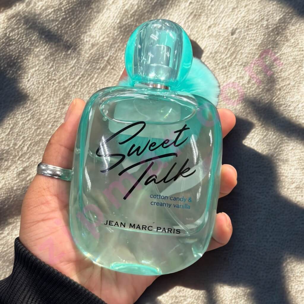 Hand holding a turquoise 'Sweet Talk' perfume bottle by Jean Marc Paris on a textured surface.