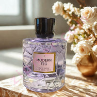 Thumbnail for Perfume bottle labeled 'Modern Fig' on a surface with flowers in the background