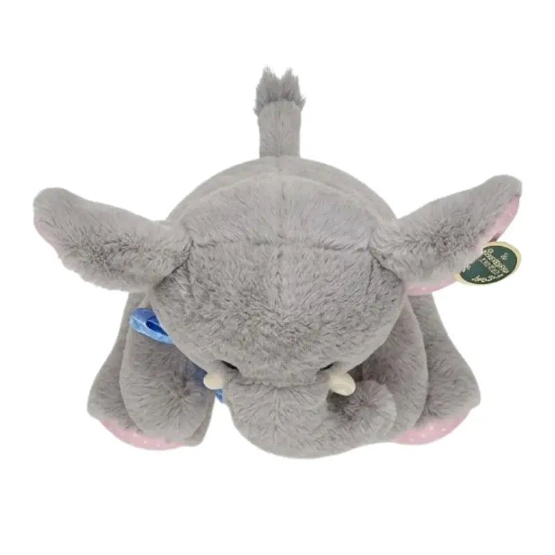 Gray elephant plush toy seen from above with floppy ears, blue bow, tusks and a tufted tail
