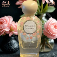 Thumbnail for Jean Rish Sugared Amber Eau de Parfum 3.4 fl oz bottle with rose print label beside pink roses