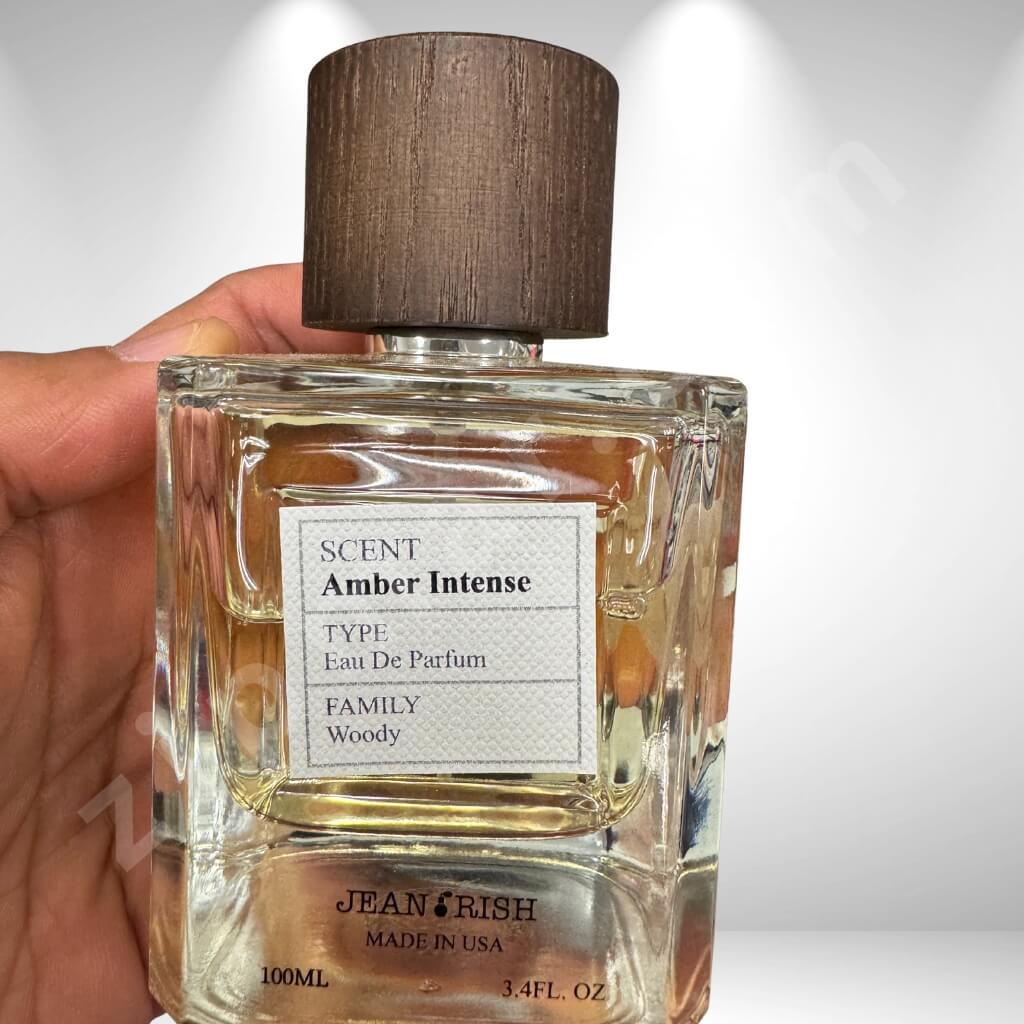 Perfume bottle labeled 'Scent Amber Intense' held by a hand on a white background