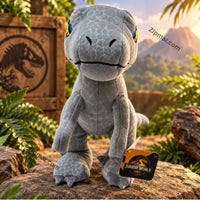 Thumbnail for Jurassic World Blue velociraptor plush toy in jungle editorial setting posed on rocks with Jurassic World crate logo background tropical foliage and volcano golden sunset light official Jurassic World hang tag visible licensed dinosaur stuffed animal gift