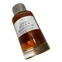 Thumbnail for Tilted front view of Le Monde Gourmand Chai Éclair Hair and Body Mist 3.4 oz bottle, highlighting the warm amber-colored liquid.