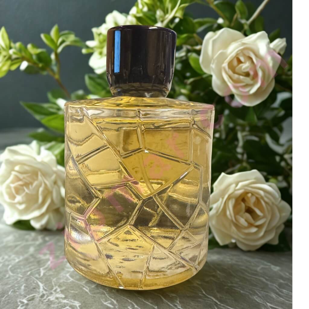 Decorative glass bottle with geometric pattern on a surface with white flowers in the background