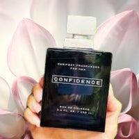 Thumbnail for Black perfume bottle labeled 'Confidence' held in front of pink flowers