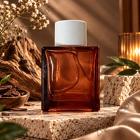 Thumbnail for Mindful Moment Eau de Parfum dark amber sculpted glass bottle with white cap on travertine stone surface driftwood bark, dried white flowers, cinnamon sticks and satin silk fabric in warm amber lifestyle setting