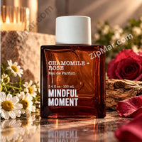 Thumbnail for Tru Fragrance & Beauty Mindful Moment Chamomile + Rose Eau de Parfum 3.4 fl. oz. dark amber glass bottle with white cylindrical cap surrounded by chamomile daisies and red roses in warm candlelight on stone surface hero lifestyle