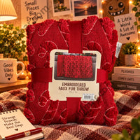 Thumbnail for Northwest embroidered faux fur throw in red in its ribbon band packaging on a plaid blanket