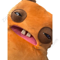 Thumbnail for Close-up of orange monster plush face showing mismatched brown eyes, pink open mouth, and two front buck teeth