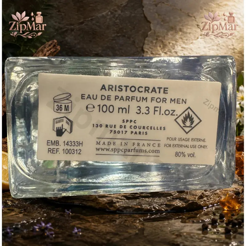 Straight-on view of Aristocrate EDP bottle on natural stone slab with white flowers and amber accents