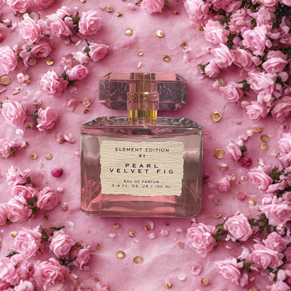 Perfume bottle labeled 'Pearl Velvet Fig' surrounded by pink flowers on a pink background