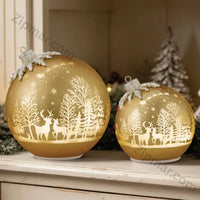 Thumbnail for Set of 2 gold glass ornament decor pieces glowing on a white shelf with a frosted tree and greenery