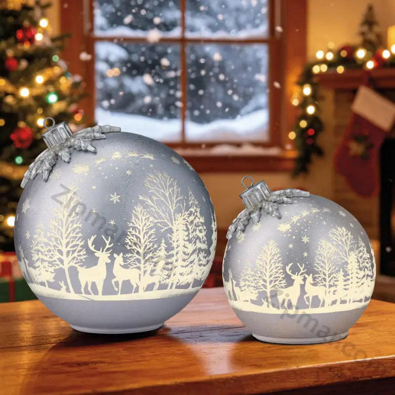 Set of 2 silver glass ornament decor pieces glowing on a wooden table with Christmas tree and window behind