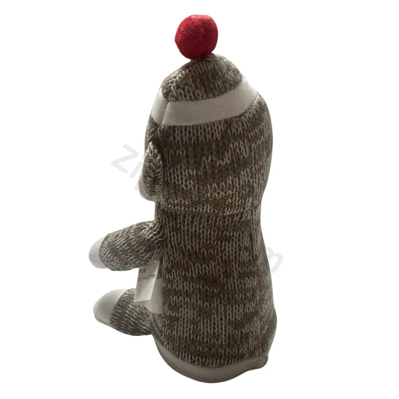 Sock monkey plush toy side and back view in marled brown knit with a red pom pom and a hang tag